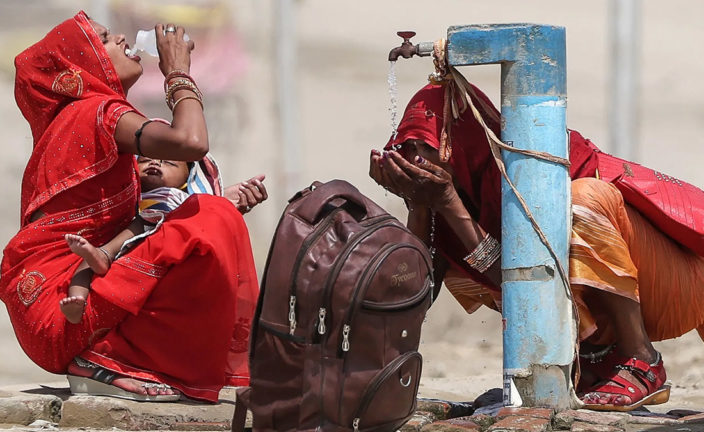 Dos mujeres beben agua en una fuente, en la India.