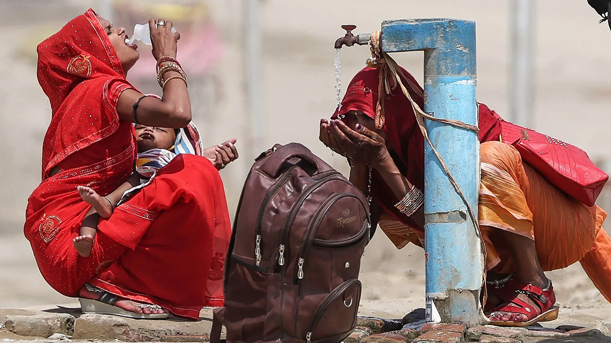 Dos mujeres beben agua en una fuente, en la India.